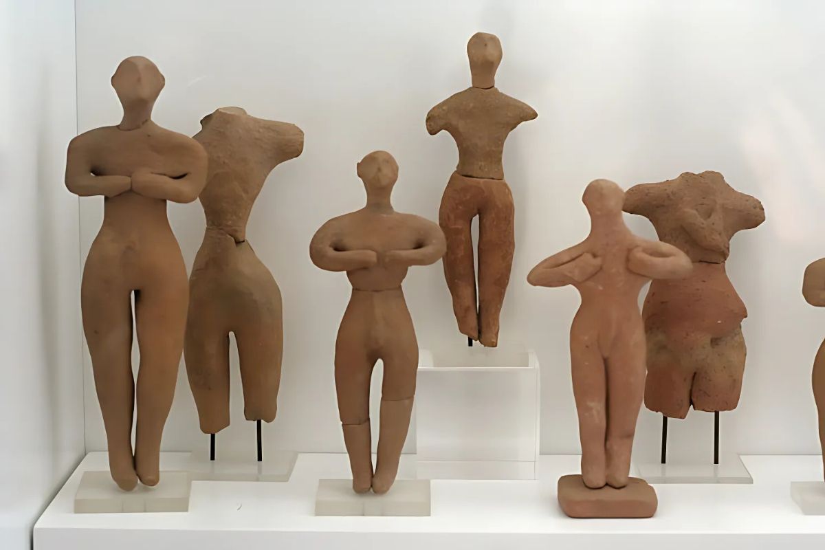 Alt text: "A collection of terracotta figurines representing Minoan worshippers with simplified human forms, displayed in a museum setting."