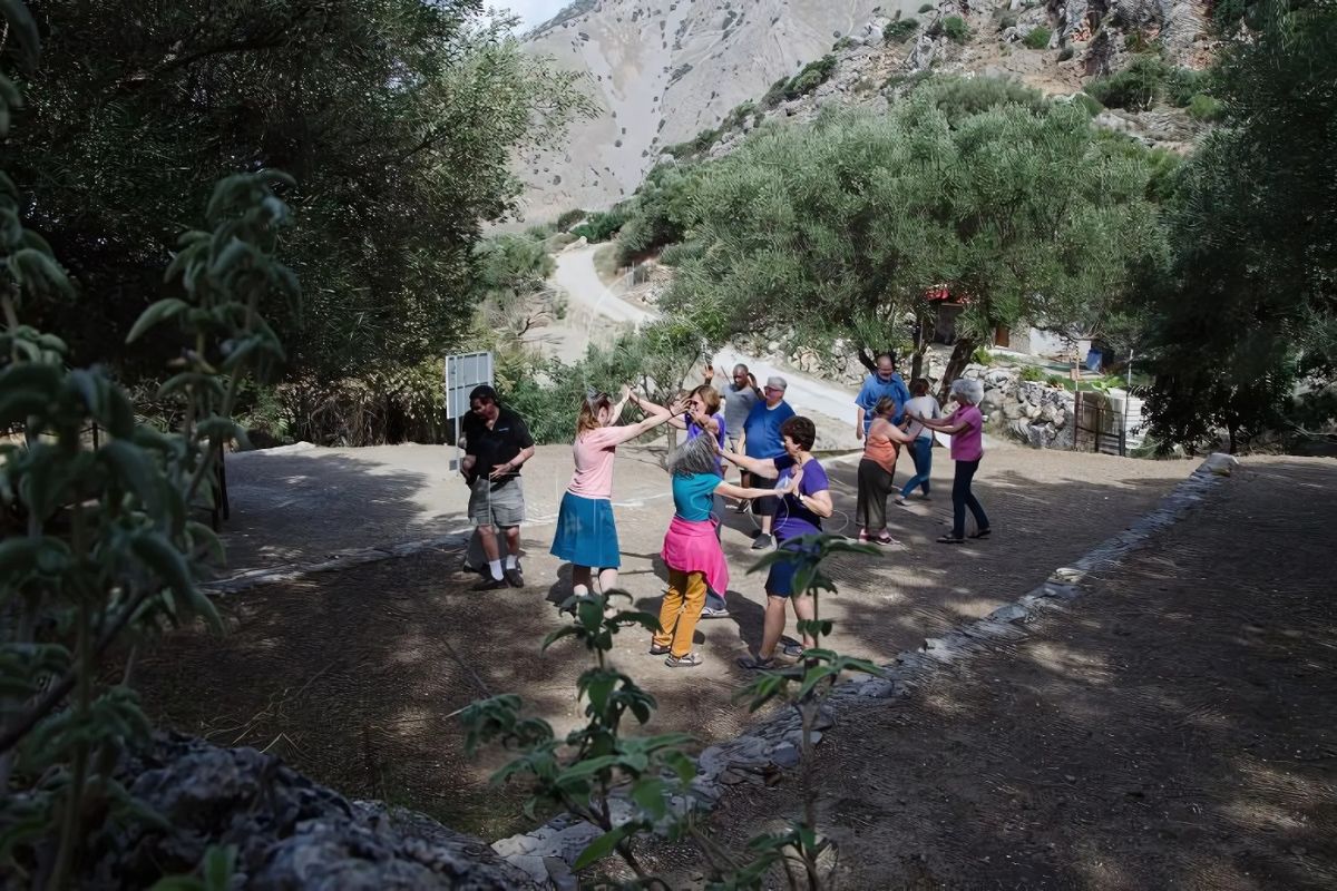Alt text: "A group of participants engaged in a nature dance experience outdoors, surrounded by trees and mountainous scenery, part of an activity by Elissos Travelling Philosophy."