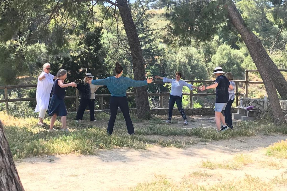 Alt text: "A group of people participating in a nature dance experience outdoors, surrounded by trees and greenery, as part of an activity by Elissos Travelling Philosophy."