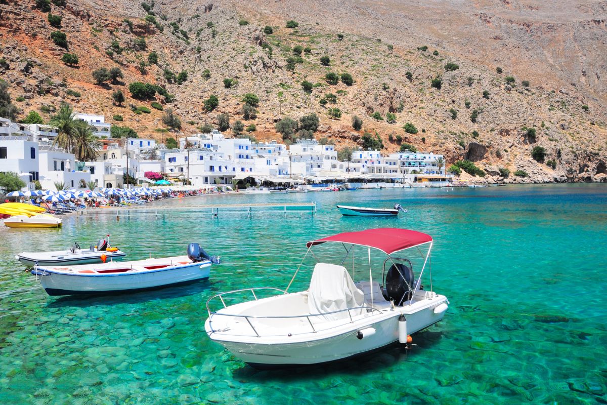 Crystal-clear waters and small boats in the traditional seaside village of Loutro in Sfakia, Crete, with whitewashed houses along the coast.