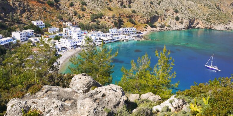 Traditional Crete village of Loutro in Sfakia, featuring whitewashed houses, turquoise sea, and a sailing boat in a peaceful bay.