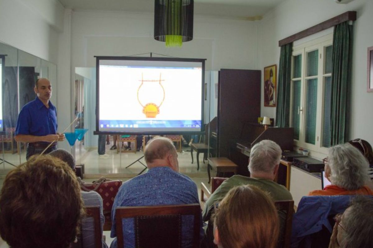 Instructor presenting to a small group in a room during an ancient Greek music lab in Crete, with a lyre diagram displayed on a projector screen.