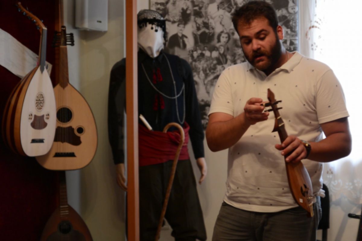 Man demonstrating a traditional string instrument during a lyre experience in Crete, with musical instruments and cultural items in the background.