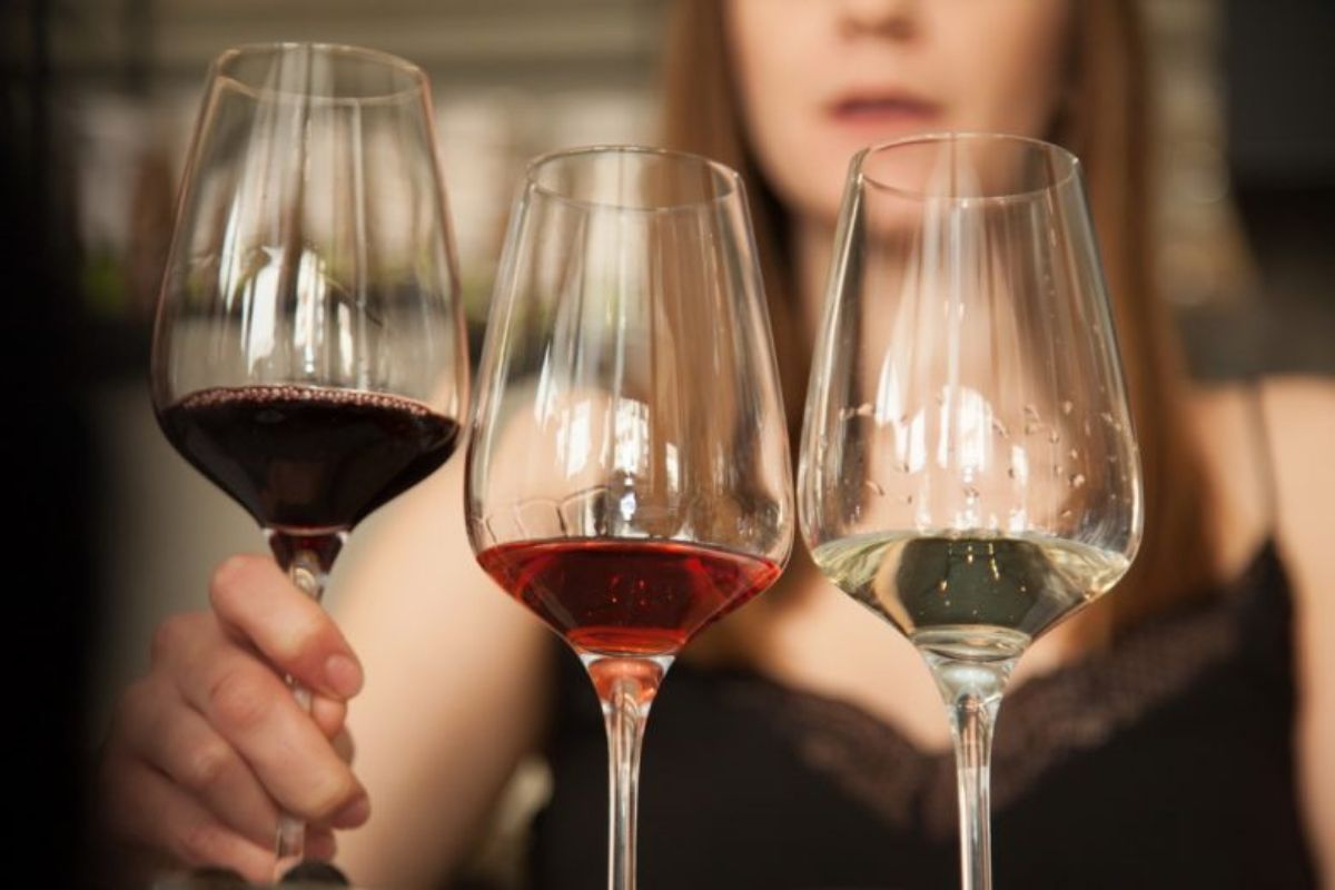 A woman holding three wine glasses filled with red, rosé, and white wine during a wine tasting experience in Crete.