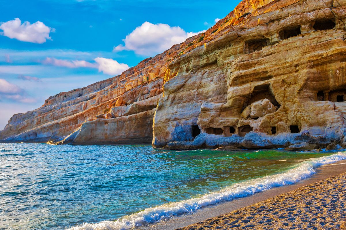 Matala Beach in Crete with cliffside caves and clear blue waters.