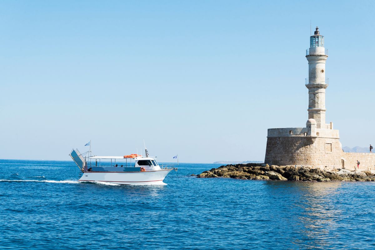 Boat sailing near the historic lighthouse in Chania, Crete during summer.