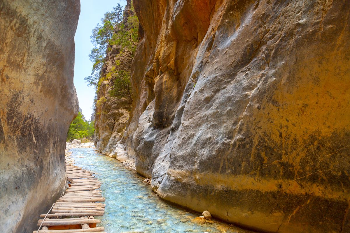 Wooden footpath along a clear stream between high canyon walls in Samaria Gorge, one of the most famous Crete gorges to hike.