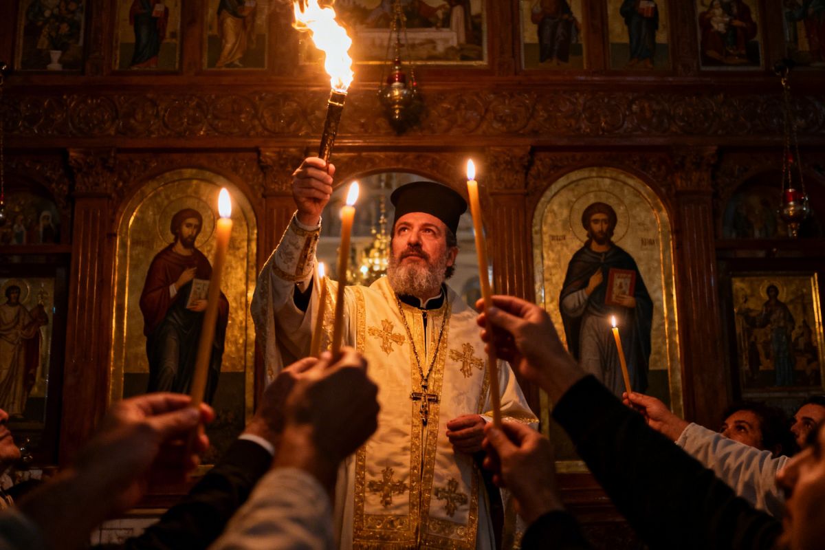 Greek Orthodox priest holding the Holy Flame during the midnight Resurrection service in a Cretan church, surrounded by candlelight, icons, and worshippers during Easter in Crete.