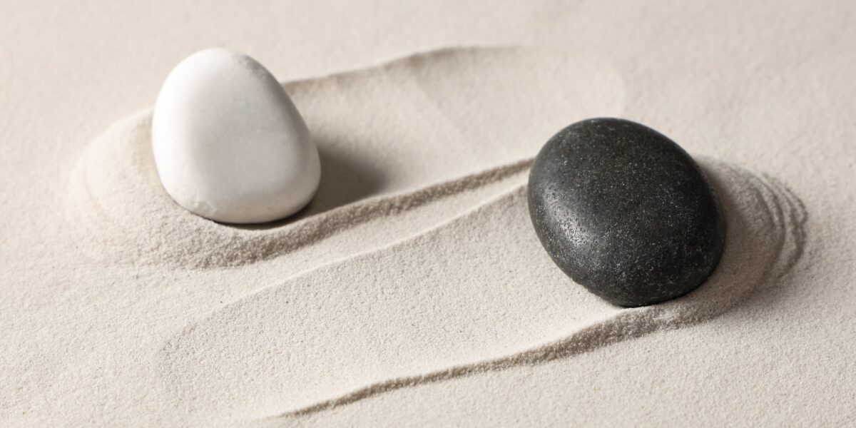 Yin og yang symbol concept with black and white stones balanced on sand.