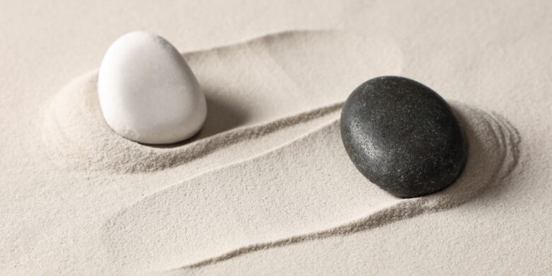 Yin og yang symbol concept with black and white stones balanced on sand.