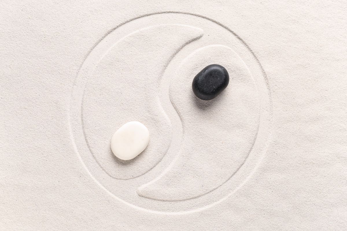 Yin og yang symbol in sand with black and white stones.