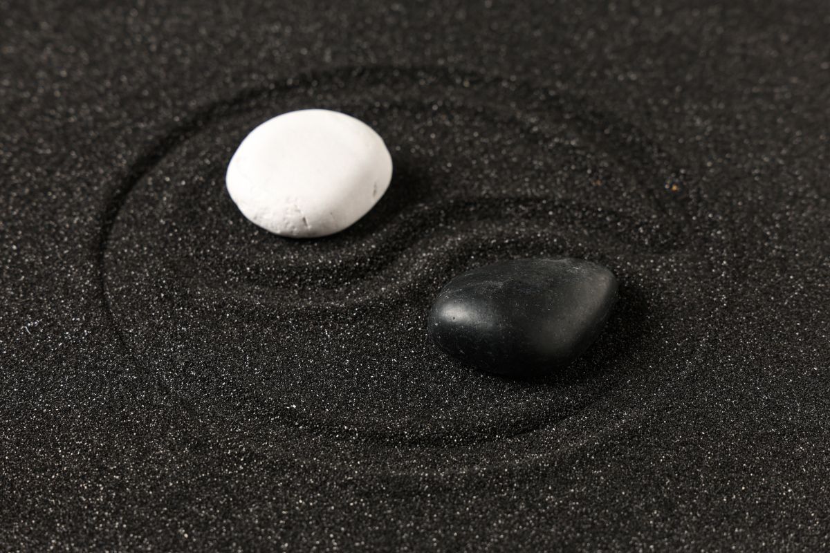 Black and white stones forming a yin og yang symbol in sand.