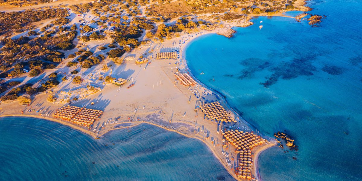 Aerial view of a curved beach lined with umbrellas and clear blue water.