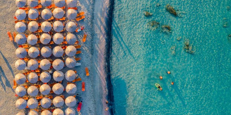 Aerial view of a beach with thatched umbrellas and clear turquoise waters.