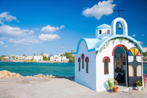 A small white and blue chapel by the sea with a clear blue sky in the background.