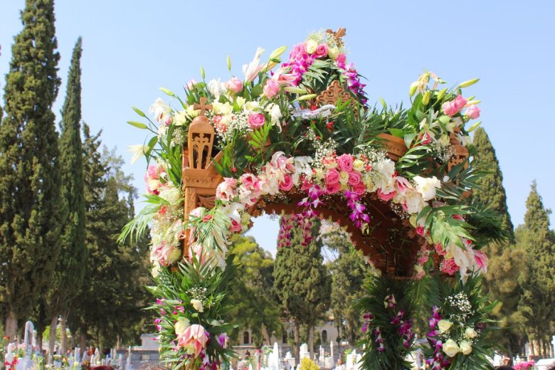 An ornately decorated floral arch with various pink and white flowers, set against a backdrop of tall trees under a clear sky.