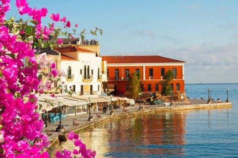 A waterfront promenade with colorful buildings and blooming flowers, overlooking a calm sea.