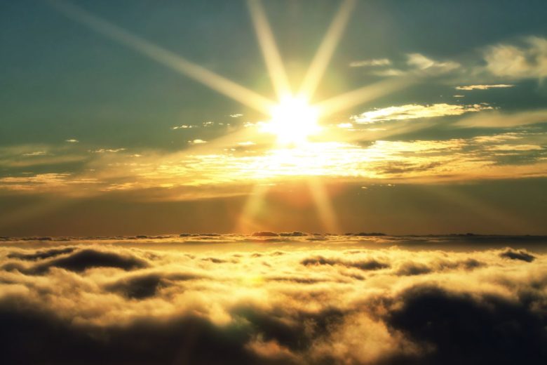 Sunrise over a sea of clouds with rays of light piercing through.