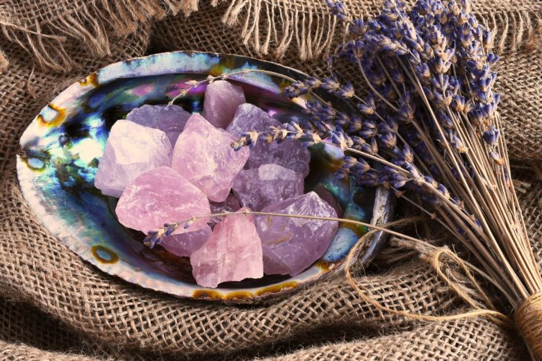 An image featuring rough rose quartz crystals in an iridescent shell, accompanied by a bundle of lavender on a burlap surface.