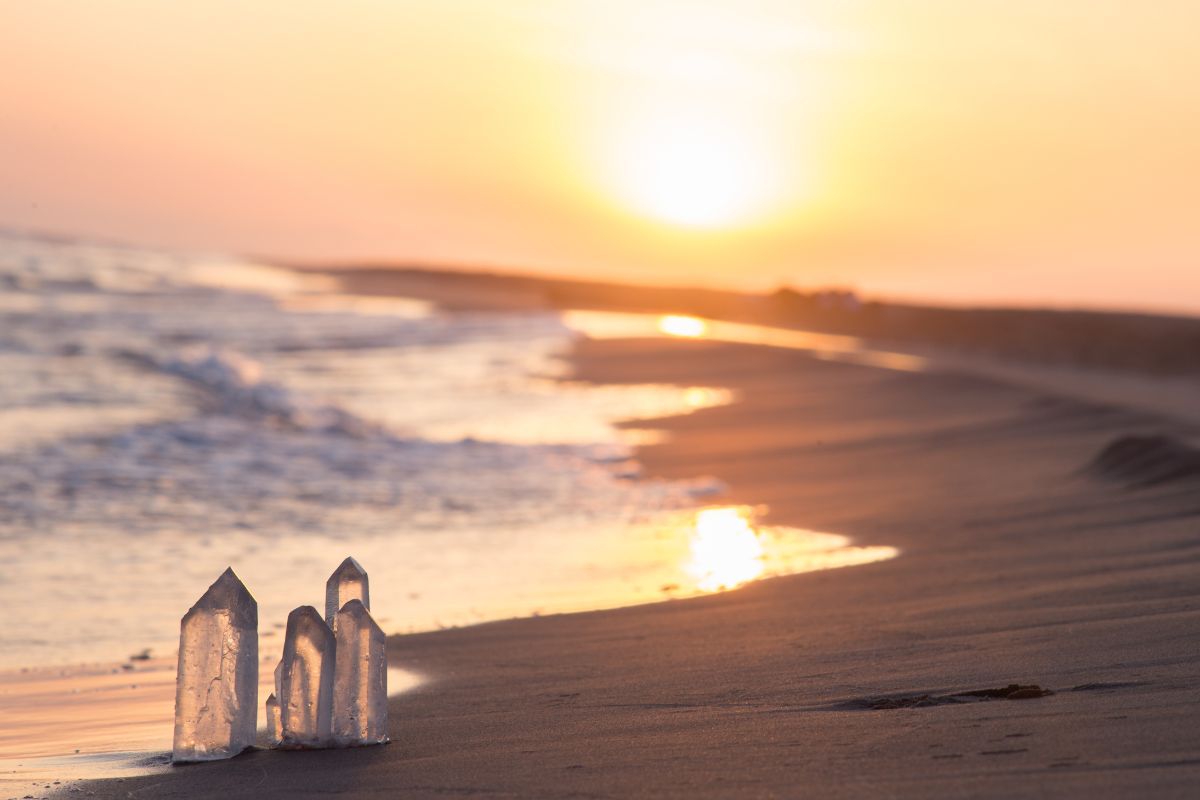 Crystal stones on a quiet beach at sunset, symbolizing spiritual healing and Divine Feminine awakening energy.