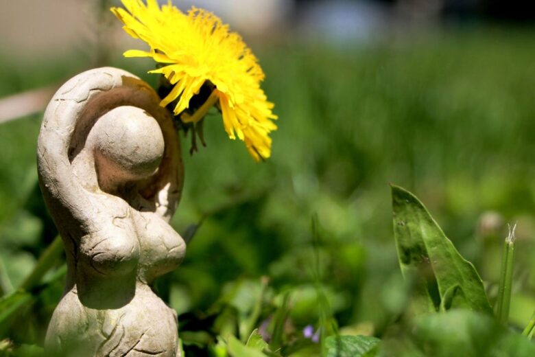 A small stone statue of a woman holding a large dandelion, set against a green grassy background.