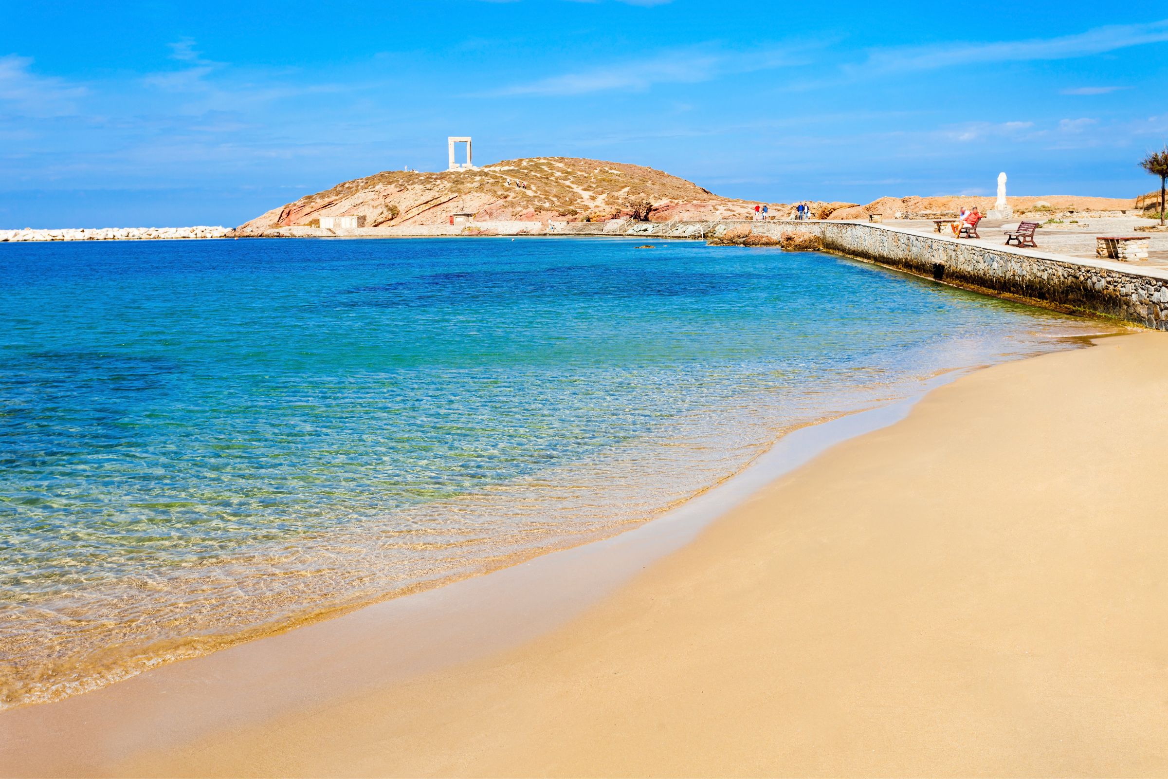 A serene view of Agios Prokopios Beach on Naxos, featuring golden sand, crystal-clear turquoise waters, and a distant view of the Portara.