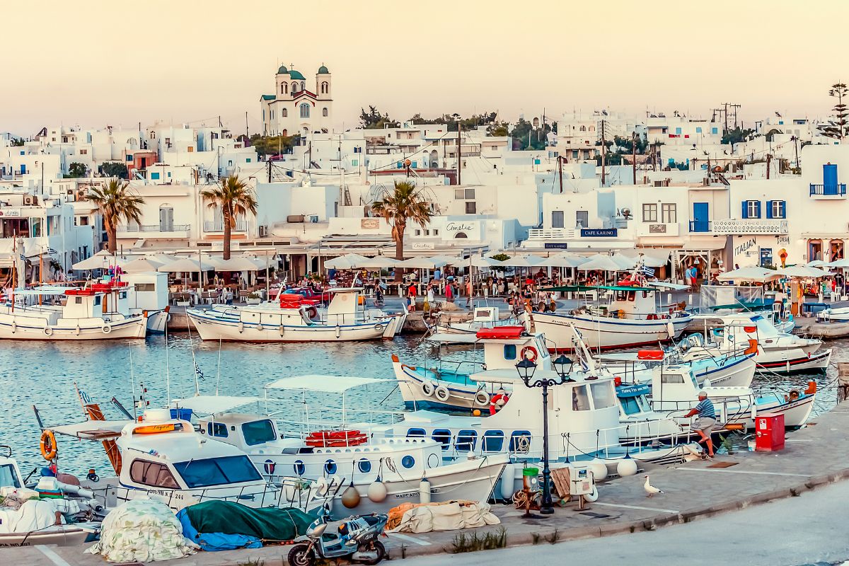 A charming waterfront scene in Paros, Greece, featuring traditional whitewashed buildings, a picturesque harbor with colorful fishing boats, and a peaceful evening atmosphere.
