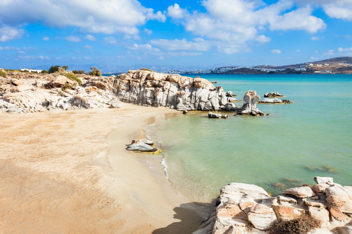 A serene beach on Paros, Greece, featuring soft sand, unique rocky formations, and clear turquoise waters under a bright blue sky.