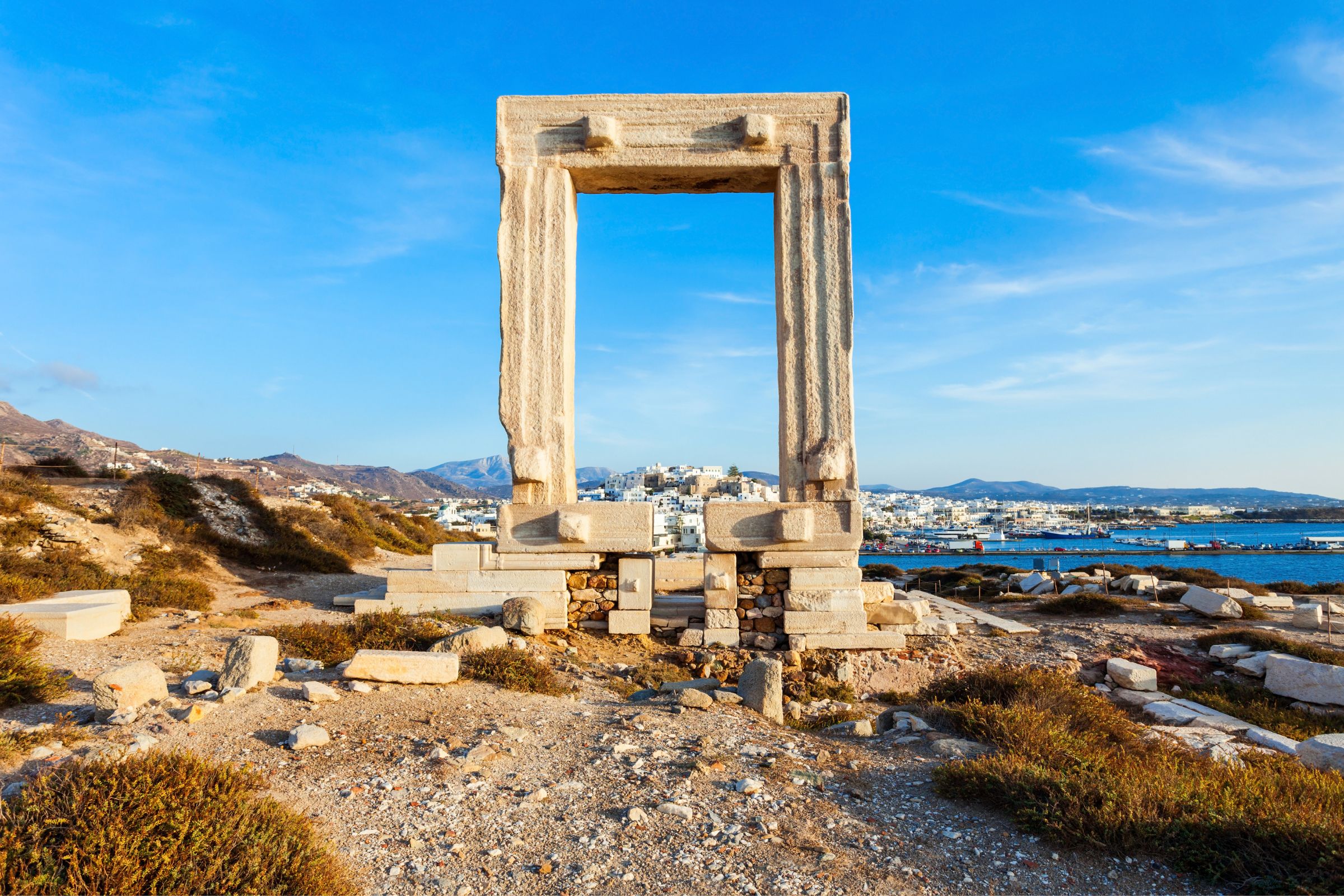 The iconic Portara on Naxos, an ancient marble gateway overlooking the island’s coastline and distant hills under a bright blue sky.