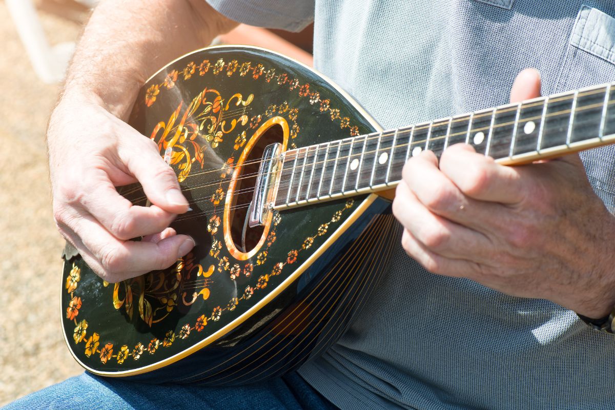 Person playing a decorated Greek bouzouki outdoors.