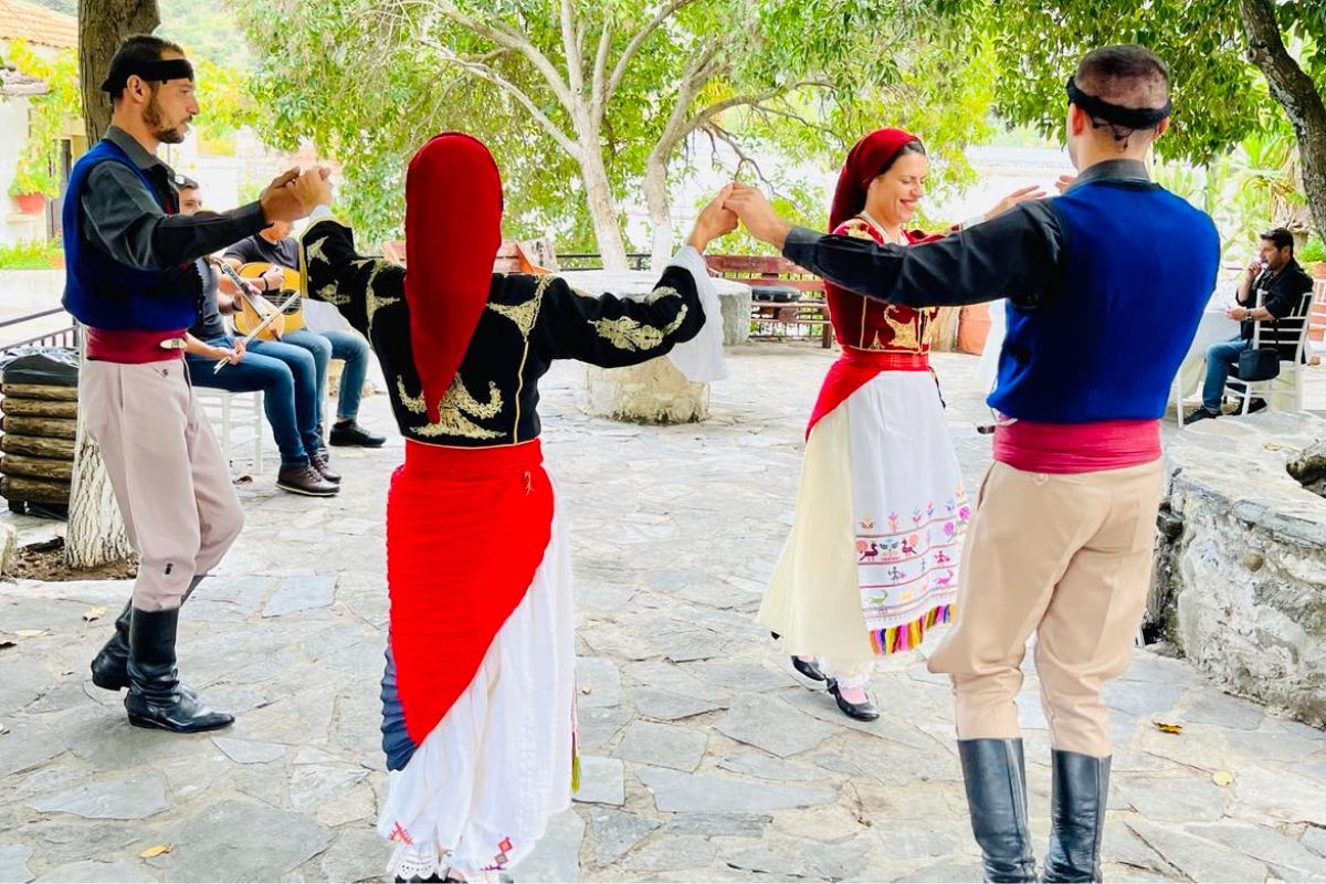 People wearing Cretan traditional dress perform a folk dance outdoors during a cultural event in Crete.