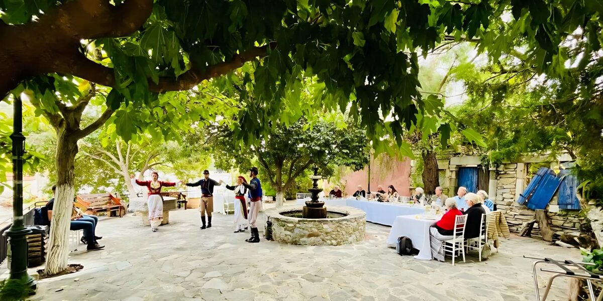 People enjoy a traditional Cretan dance performance in an outdoor courtyard, with dancers wearing Cretan traditional dress.