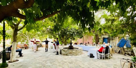 People enjoy a traditional Cretan dance performance in an outdoor courtyard, with dancers wearing Cretan traditional dress.