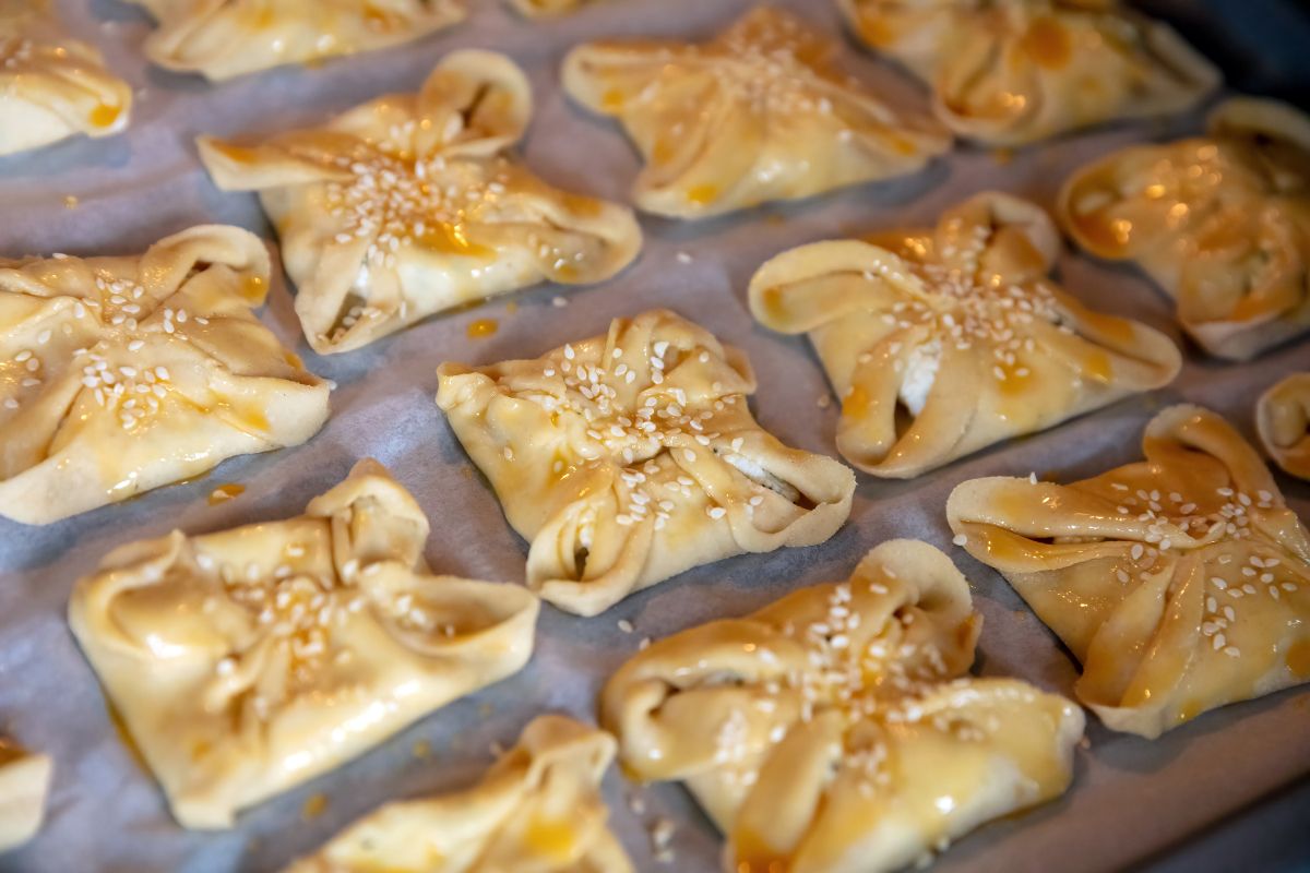 Cretan pastries kaltsounia filled with cheese and topped with sesame seeds, ready for baking.