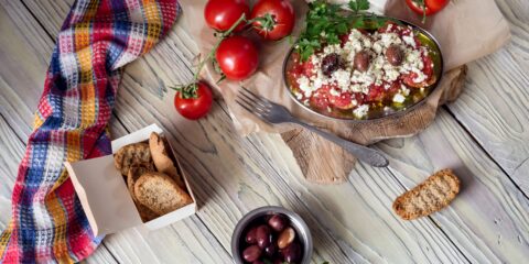 Traditional Cretan food featuring dakos with tomatoes, feta cheese, olive oil, and olives, served with barley rusks and local ingredients on a rustic table.