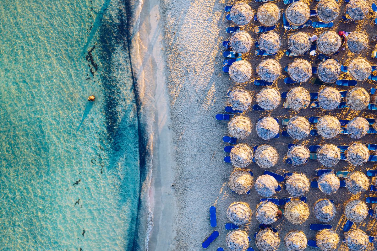 Aerial view of Elafonissi Beach in Chania, Crete, showing turquoise waters and organized sunbeds with umbrellas on the sand