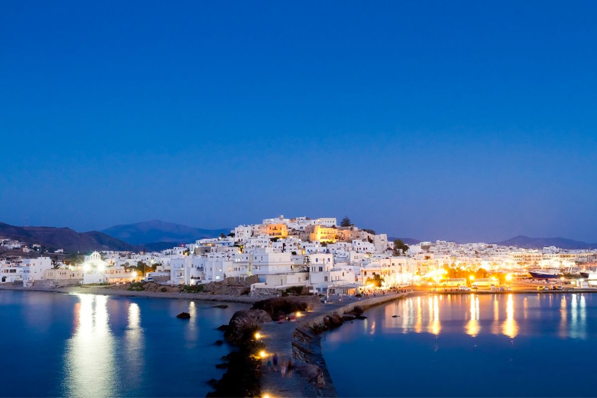 Naxos Chora at dusk with illuminated buildings and water reflections.