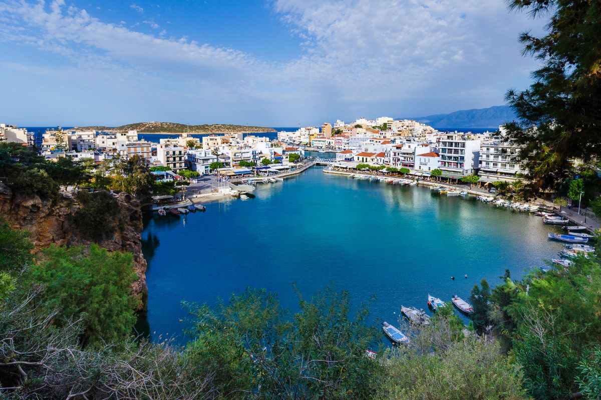 View of Agios Nikolaos in Crete with colorful buildings, calm harbor waters, and small boats along the waterfront.