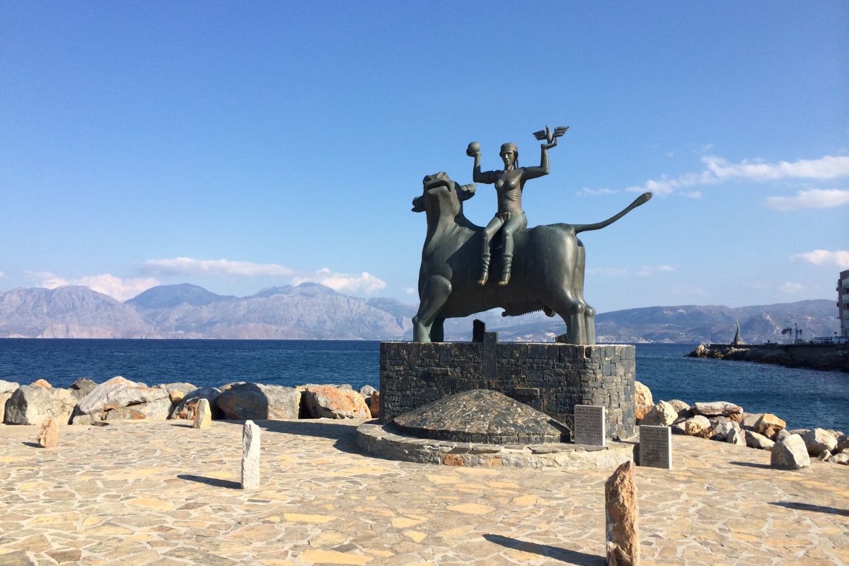 Statue of Europa in Agios Nikolaos, Crete, with sea and mountains in the background.