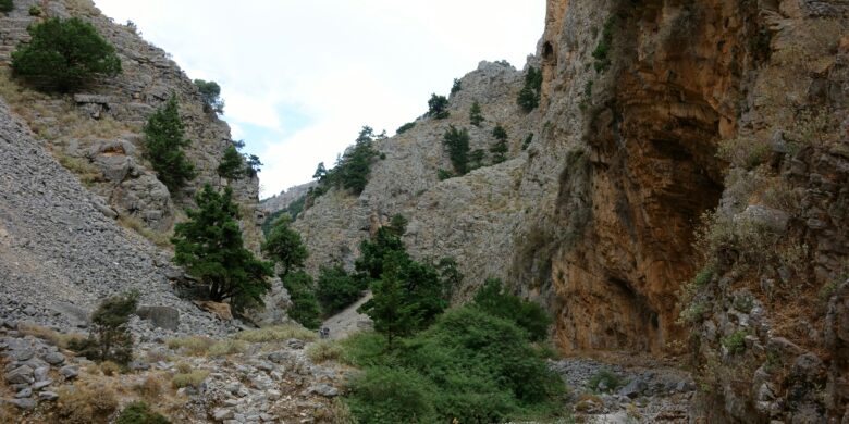 Hikers on the rocky Gorge Imbros trail in Crete, walking between steep cliffs and scattered greenery.