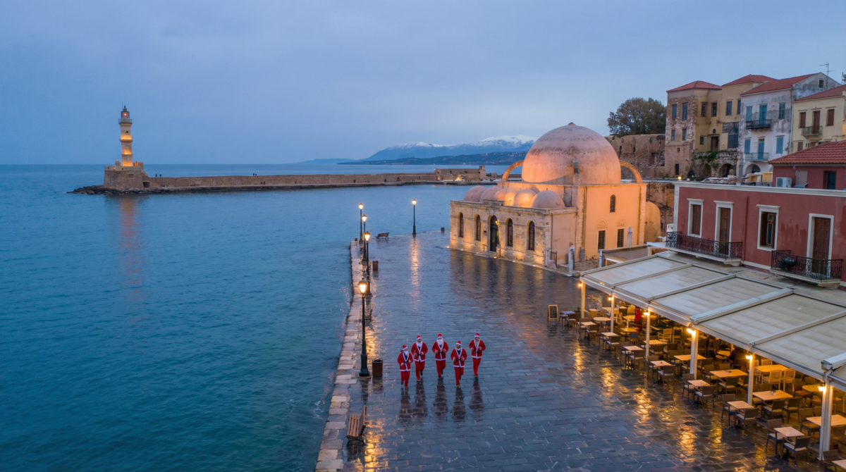 Chania Old Venetian Harbor in Crete at Christmas, with the lighthouse and a small Santa run group along the waterfront.