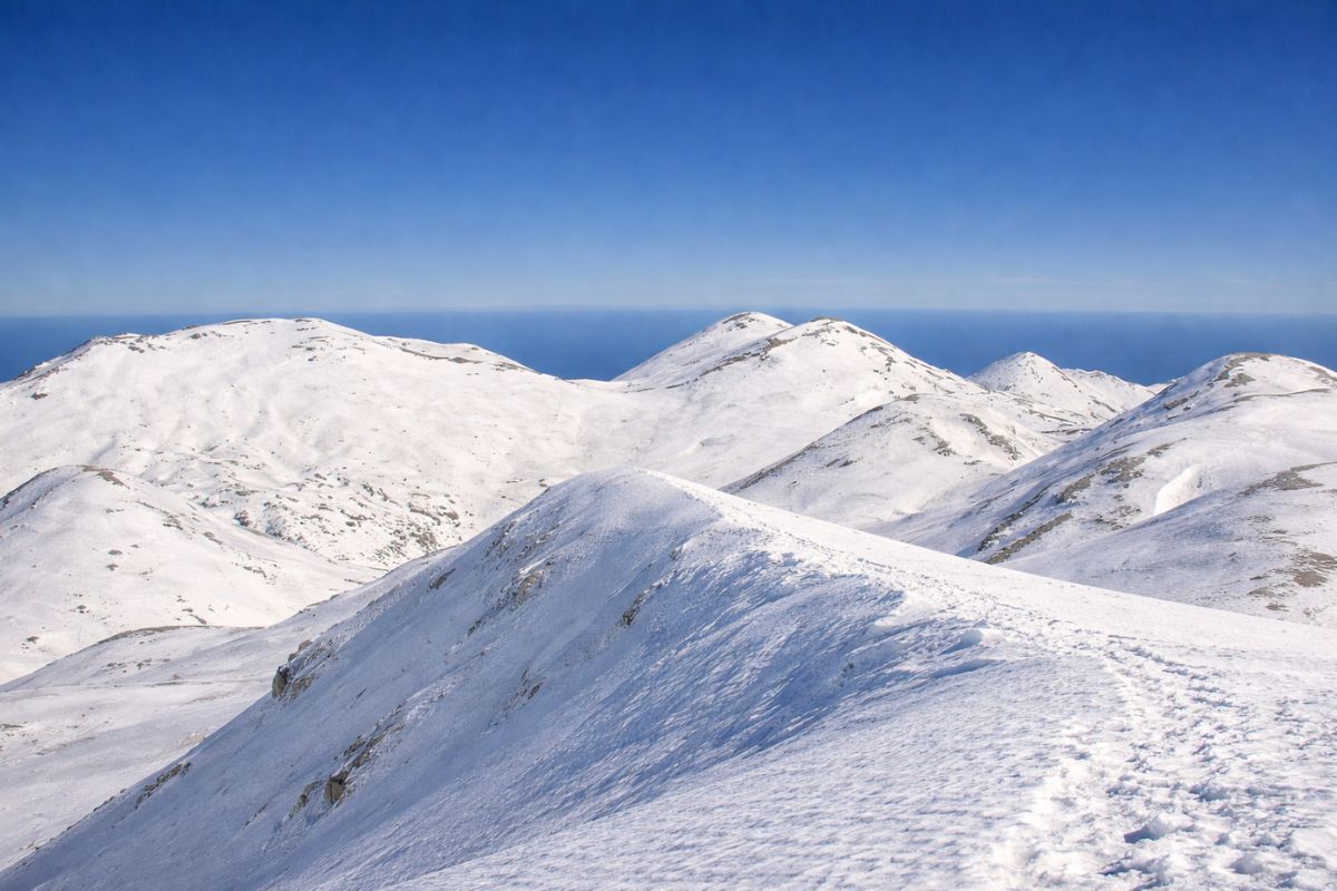 AI-generated view of Pachnes Peak in the Crete White Mountains (Lefka Ori) with snow-covered ridges and the sea beyond.
