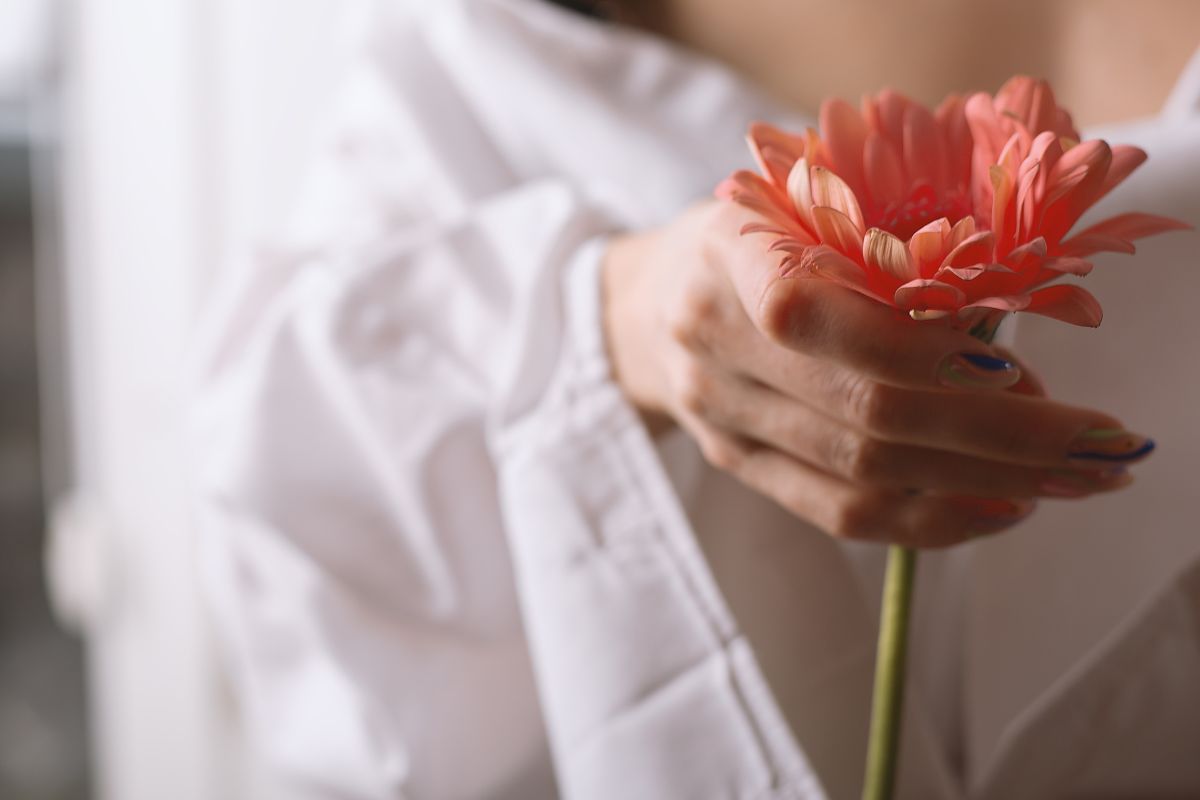 Hand holding a pink flower, symbolizing Divine Feminine Goddess energy, tenderness, and inner growth.