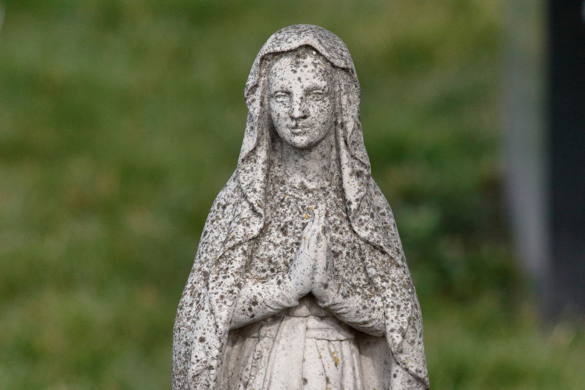 Stone statue of Mary Magdalene in prayer, reflecting Divine Feminine Goddess themes of devotion, healing, and sacred wisdom.
