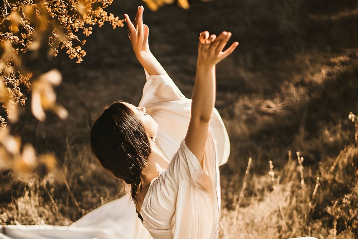 Woman in flowing dress practicing mindful movement outdoors in warm golden light.