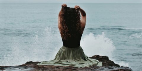 Woman seated by the sea, reflecting divine feminine divine masculine balance, emotional healing, and inner harmony.