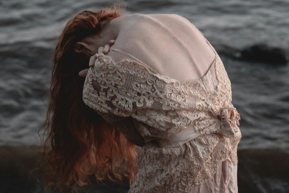 Woman in a flowing lace dress by the sea, expressing divine feminine energy, softness, and emotional awareness.