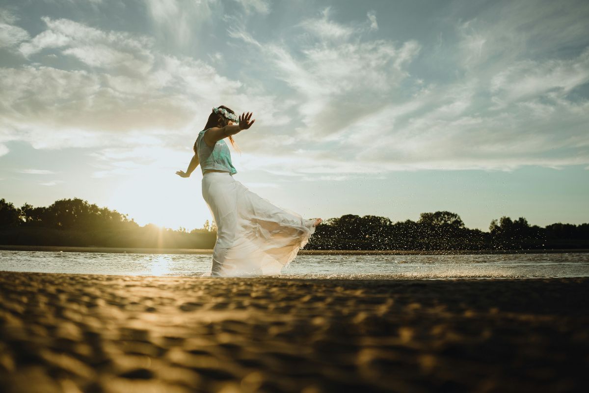Woman dancing by the water at sunset, symbolizing healing the feminine energy through freedom, embodiment, and release.