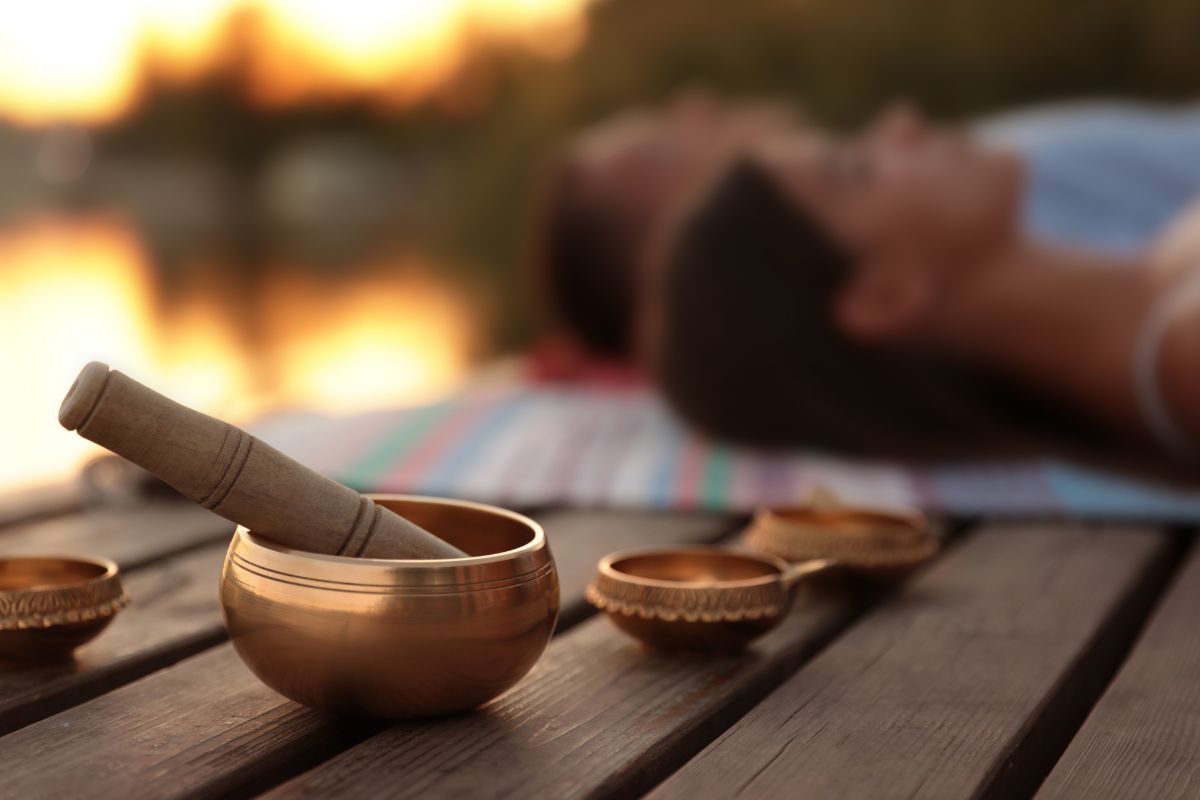 Sound healing bowls by the water at sunset, representing healing the feminine energy through rest, meditation, and inner balance.