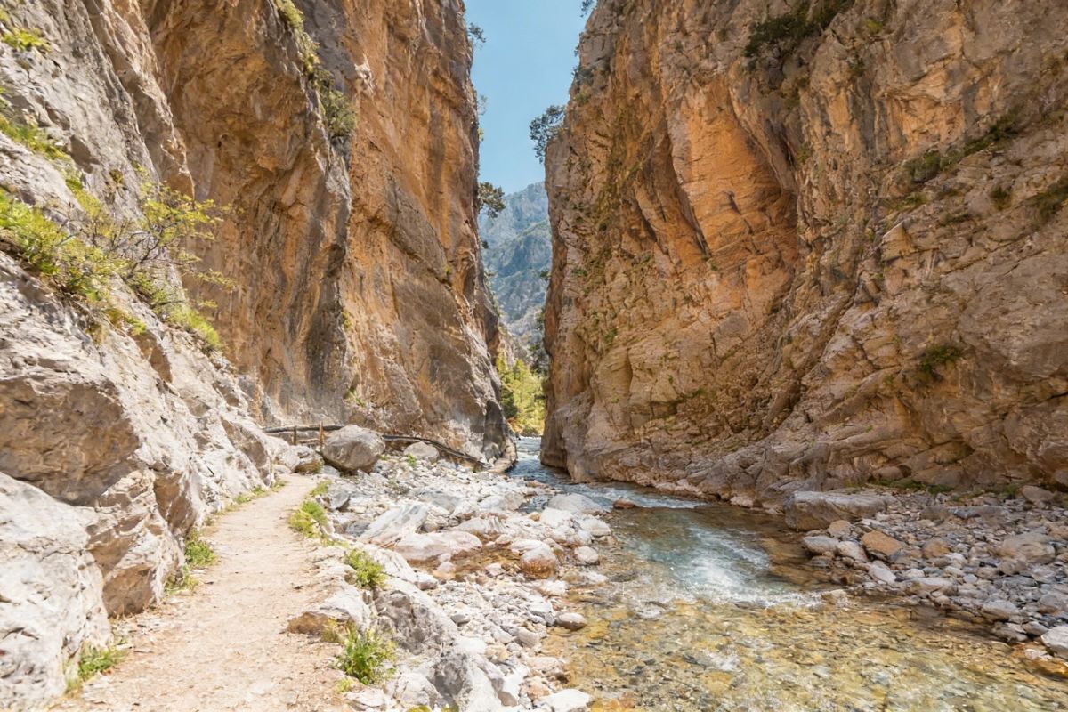 Samaria Gorge Iron Gates in Crete with towering limestone walls, rocky trail, and flowing stream.